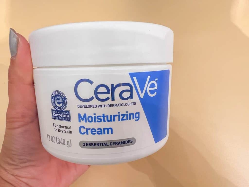 A woman's hand holding a jar of cerave moisturizing cream