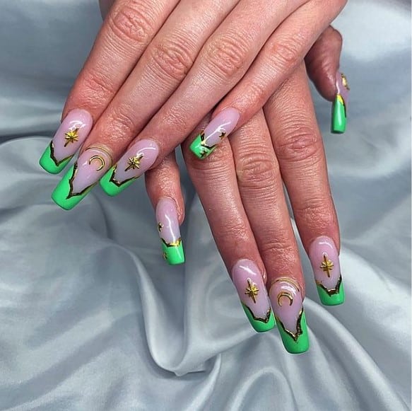 A woman's hands with purple nail polish base that has lines in chrome gold, celestial elements like stars and crescent moon designs