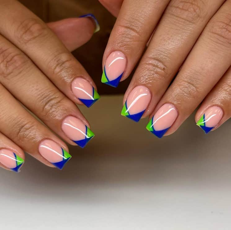 A closeup of a woman's hands with light pink nail polish that has V-shaped tips with a green-and-blue color combination