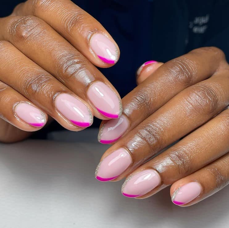 A closeup of a woman's hands with light pink nail polish base that has a hot pink and silver glitter polish on v-shaped tips 