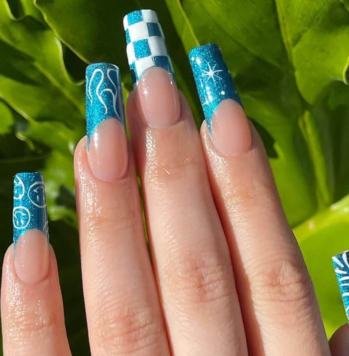A closeup of a woman's hand with white smiley faces, wavy lines, sparkling stars, and checkered patterns against a turquoise chrome background