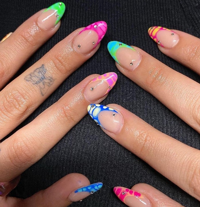A closeup of a woman's hands with a nude nail polish base that has neon and pastel hues on crocodile prints and two or three tiny rhinestones