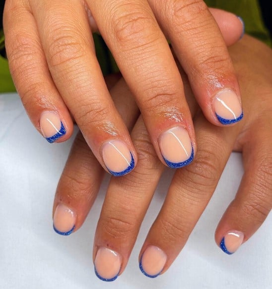 A woman's hands with short nude nails with blue french tip design