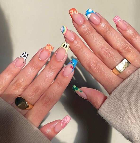 A woman's hands with colorful nail french tips and mixed designs such as Leopard prints, fruits, and flowers