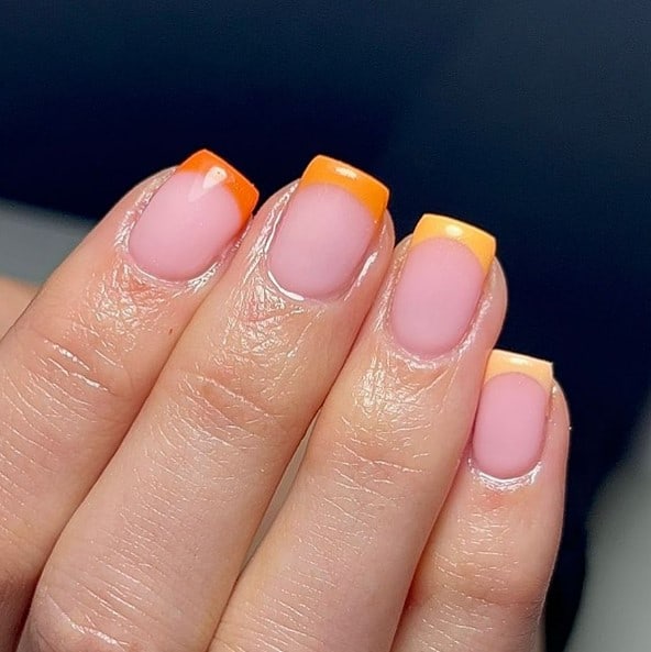 A woman's nails with shades of orange french tip design