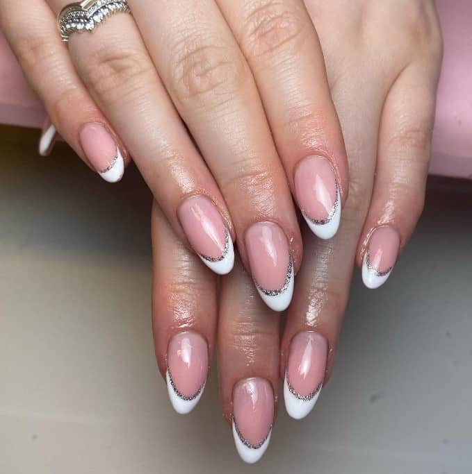 A woman's hands with natural pink nail color and has white and silver french tips
