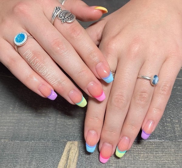 A woman's hands with rainbow colored french tip nails and rings.