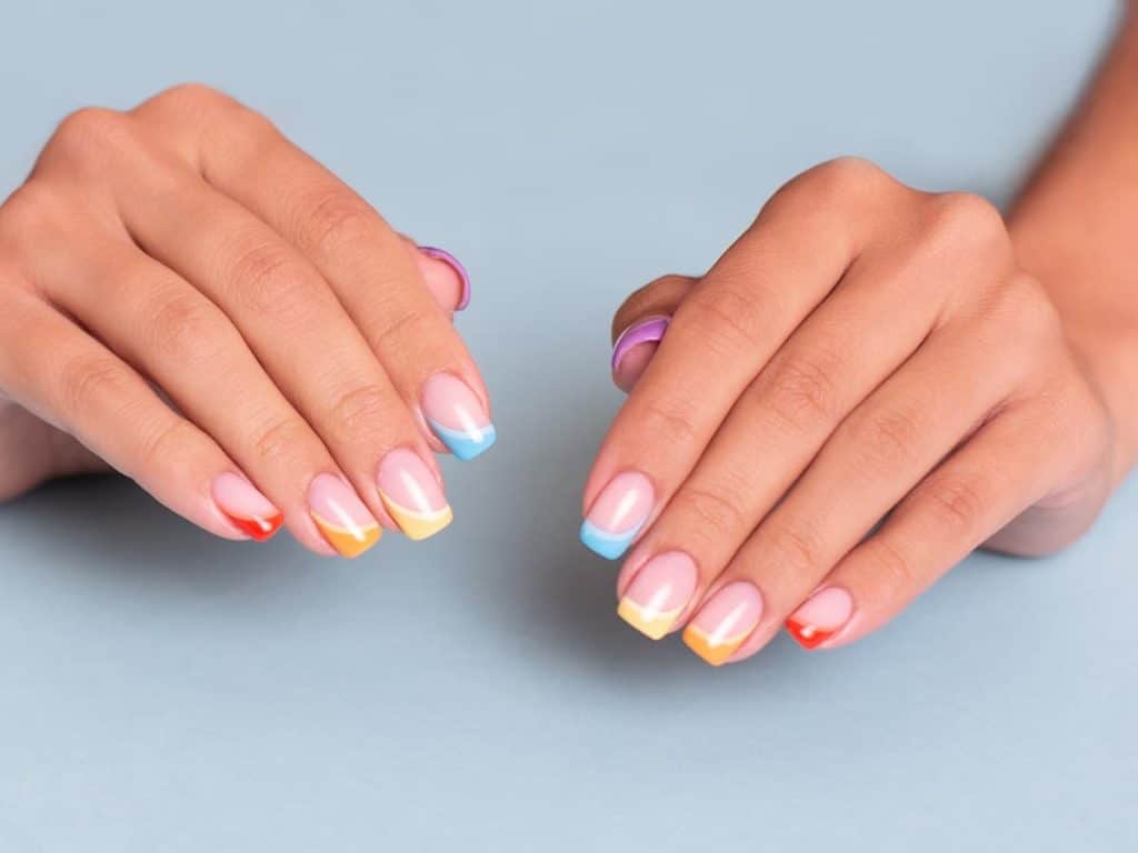 A woman's hands with colorful french tip manicures on a blue background.