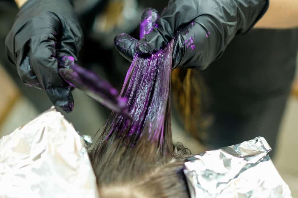 A woman is getting her hair dyed purple by a hairstylist