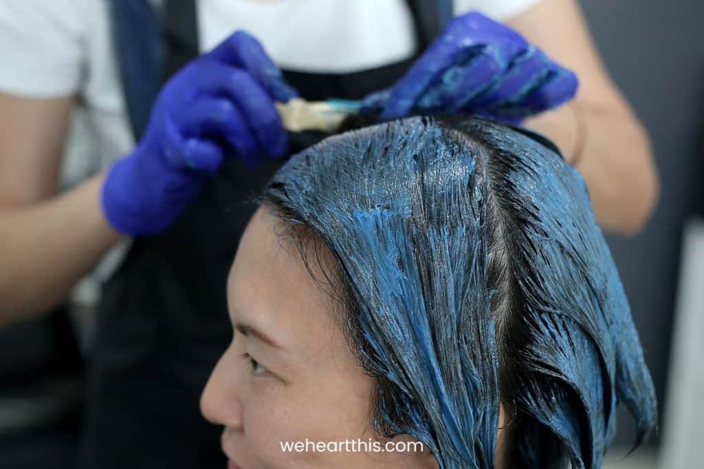 A person applying hair dye to a woman