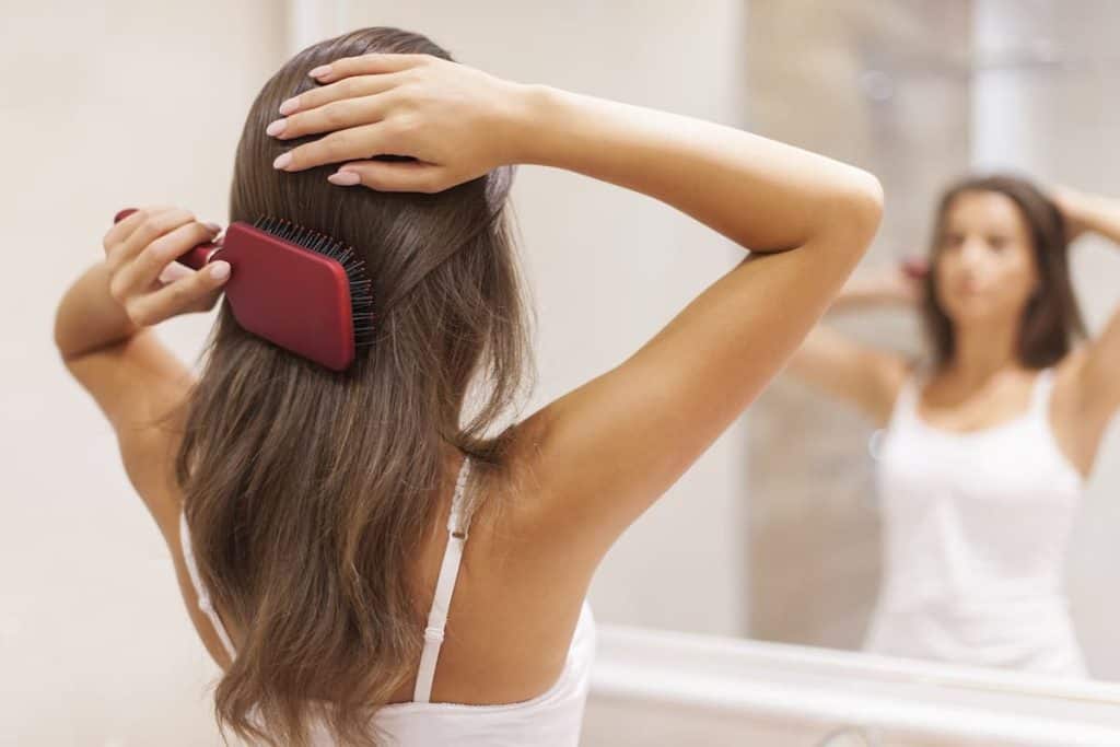 A woman combing her hair while looking at herself in the mirror