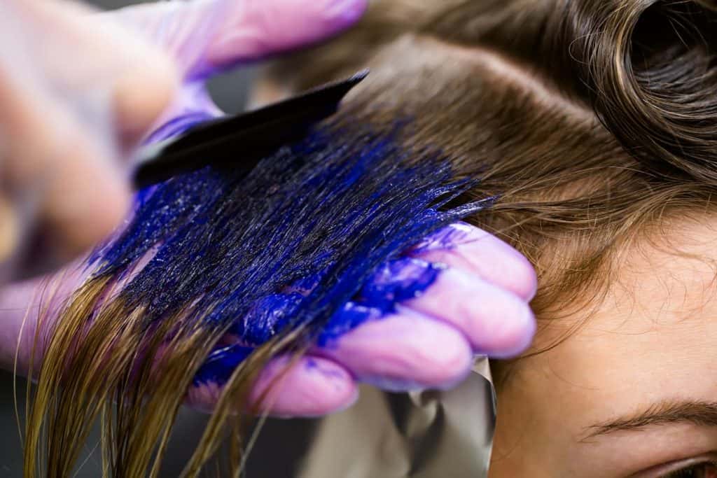 A woman is getting her hair dyed blue by a hairstylist