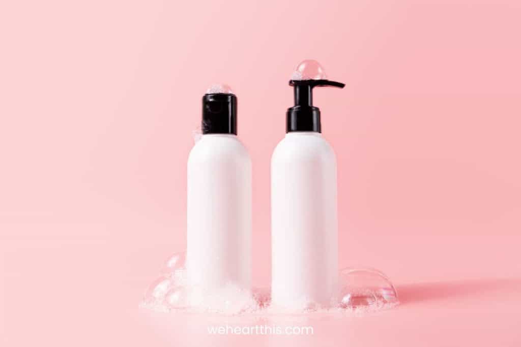 Two white bottles of shampoo and conditioner with black lids in a pink background