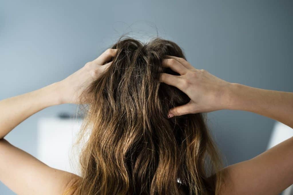 The back of the hair of a brown haired woman touching her hair because of scalp irritation