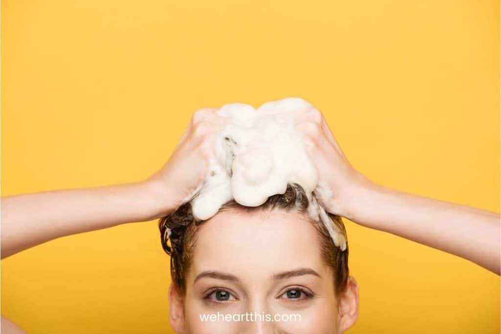 Cropped view of girl washing hair while looking at camera isolated on yellow