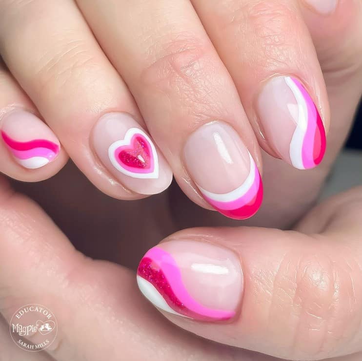 A closeup of a woman's hand with nude nail polish base that has swirls and glittery hearts in hot pink, candy pink, and white pop