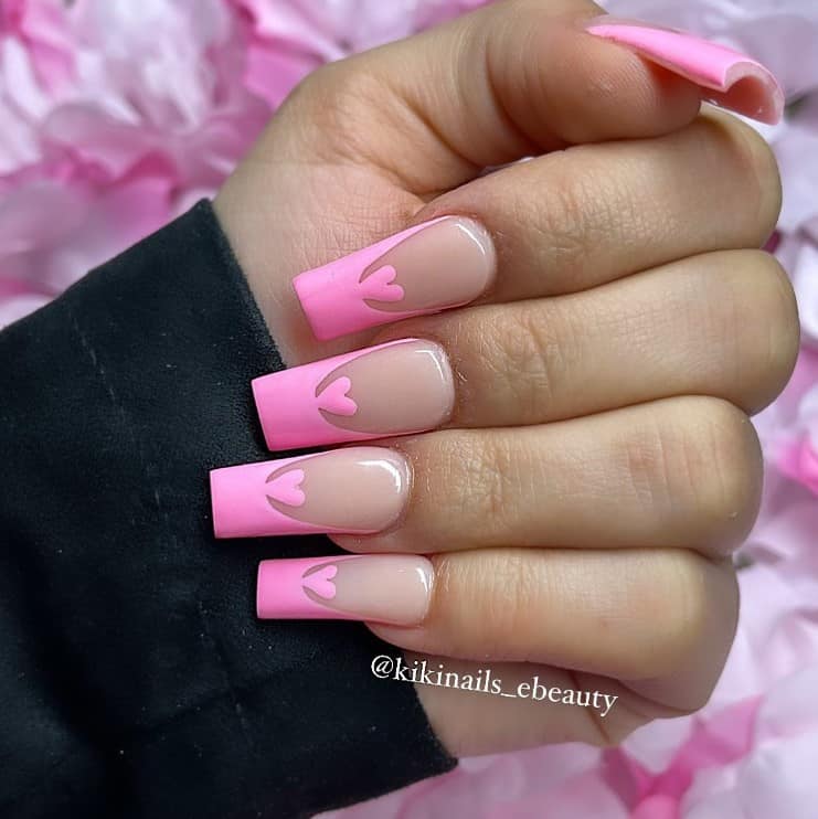 A closeup of a woman's hand with nude nail polish that has pink tips and hearts