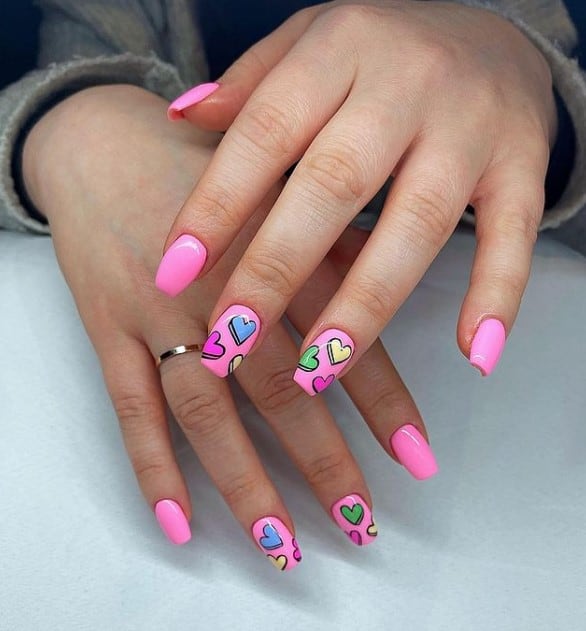 A closeup of a woman's hands with pink nail polish that has heart nail design on select nails