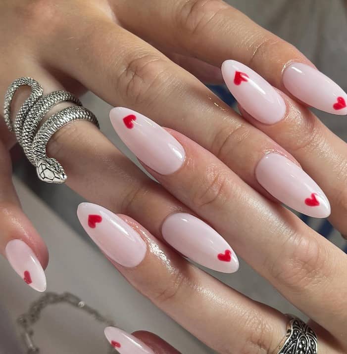A closeup of a woman's hands with light pink nail polish that has small red hearts nail designs