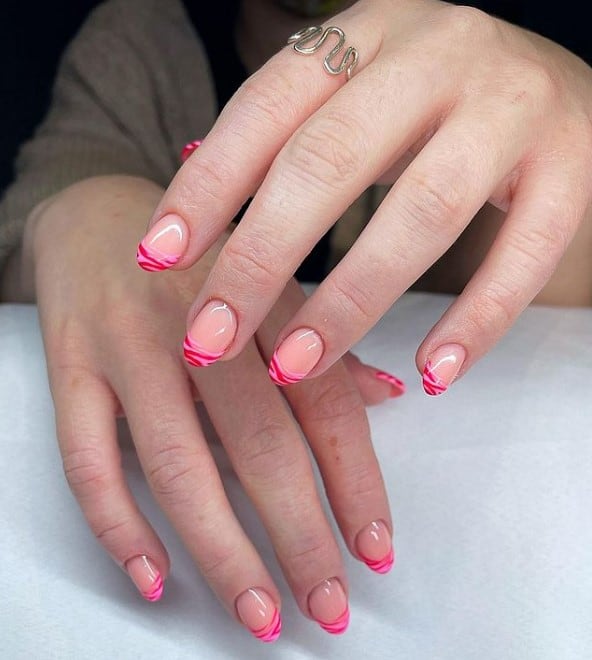 A closeup of a woman's hands with glossy peach nail polish base that has fuchsia pink swirls