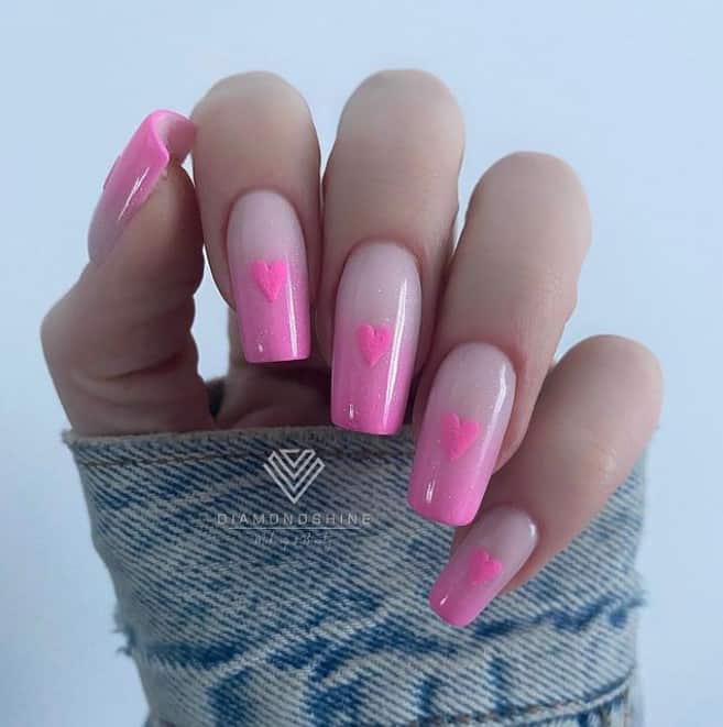 A closeup of a woman's hand with nude nail polish that has pink tips and heart nail designs