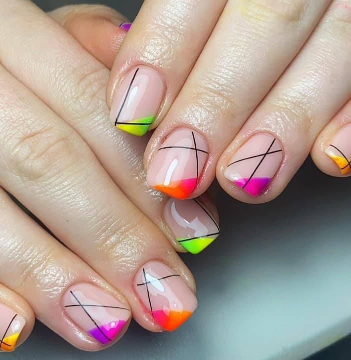 A closeup of a woman's hands with a glossy nude nail polish that has multicolored nail tips 