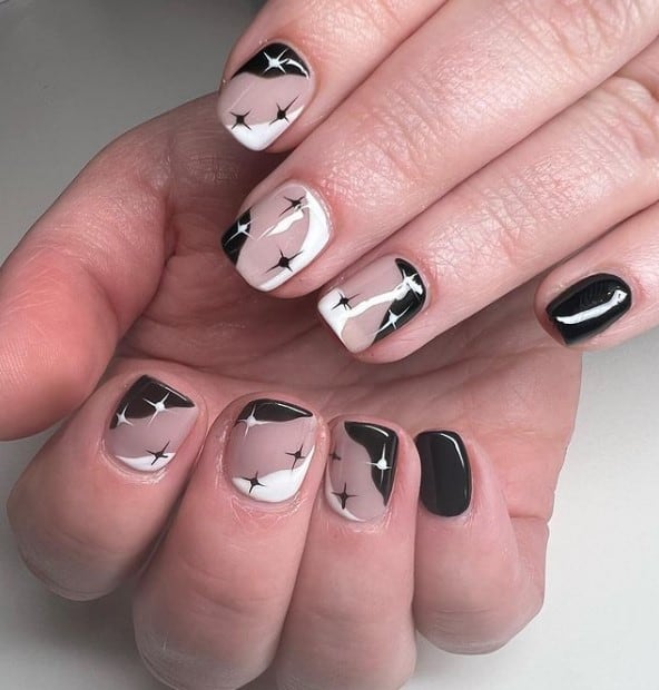 A closeup of a woman's hands with celestial black-and-white and nude nail design and polish that has star stickers