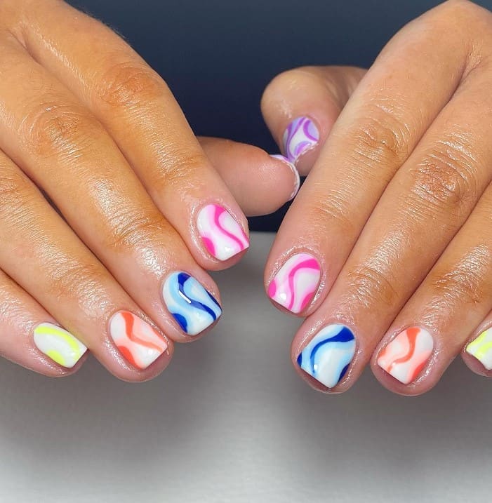 A closeup of a woman's hands with white nail polish base that has two-toned swirls in different shades of orange, pink, blue, yellow, and purple