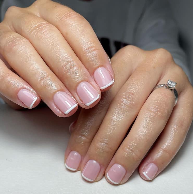 A closeup of a woman's hands with a glossy nude nail polish that has white nail tips