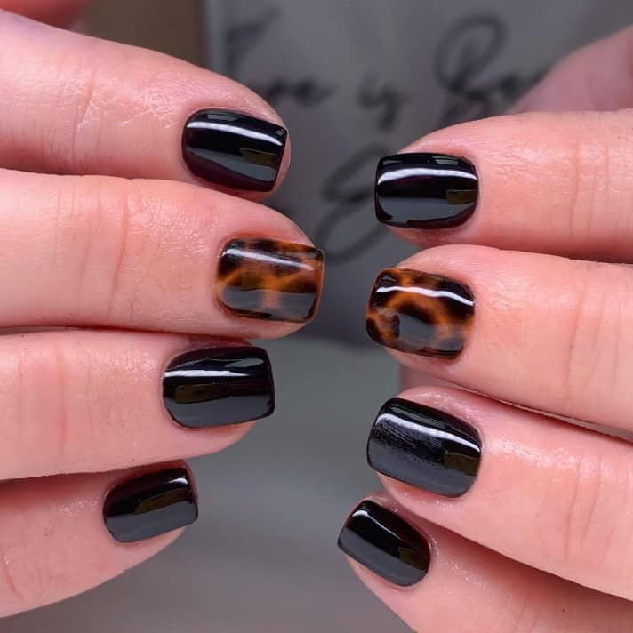 A closeup of a woman's hands with black nail polish base that has a tortoise shell design on select nails