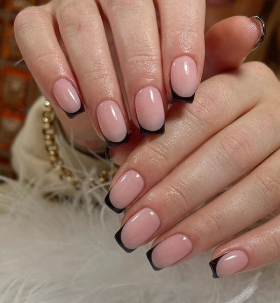 A closeup of a woman's hands with a glossy peach nail polish base that has black nail tips 