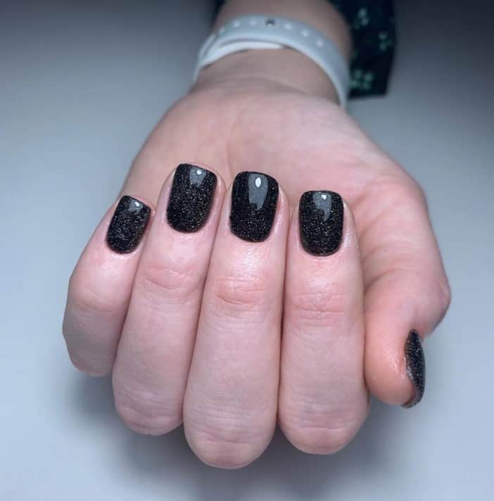 A closeup of a woman's hand with black nail polish that has glitter