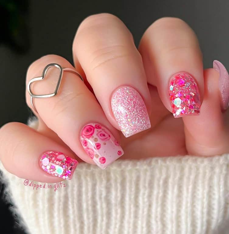 A closeup of a woman's hand with pink nail polish that has glitter and flowers bloom nail designs
