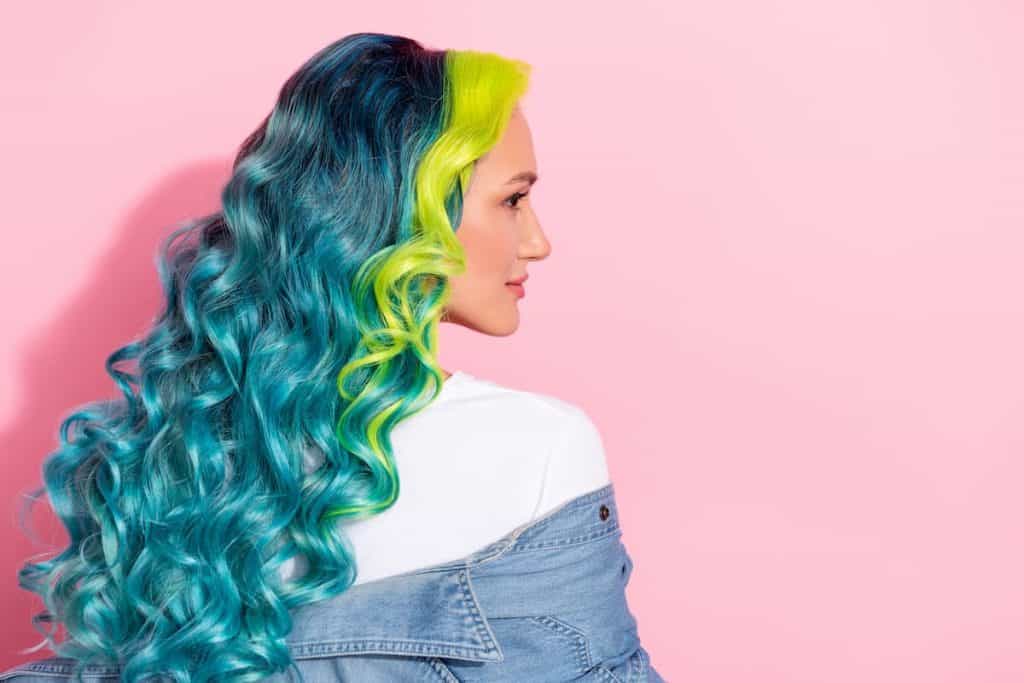 side view photo of a girl with beautiful long curled hair colored with teal and lime green highlights in front