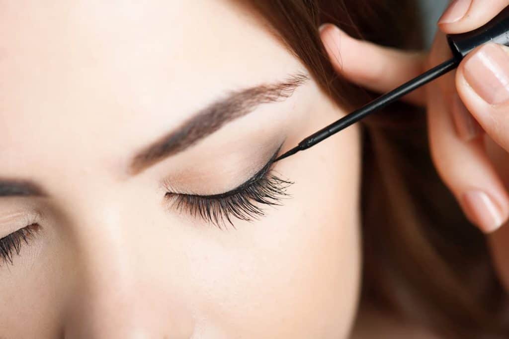 A woman is applying mascara to her eyelashes using the best eyeliner for sensitive eyes.