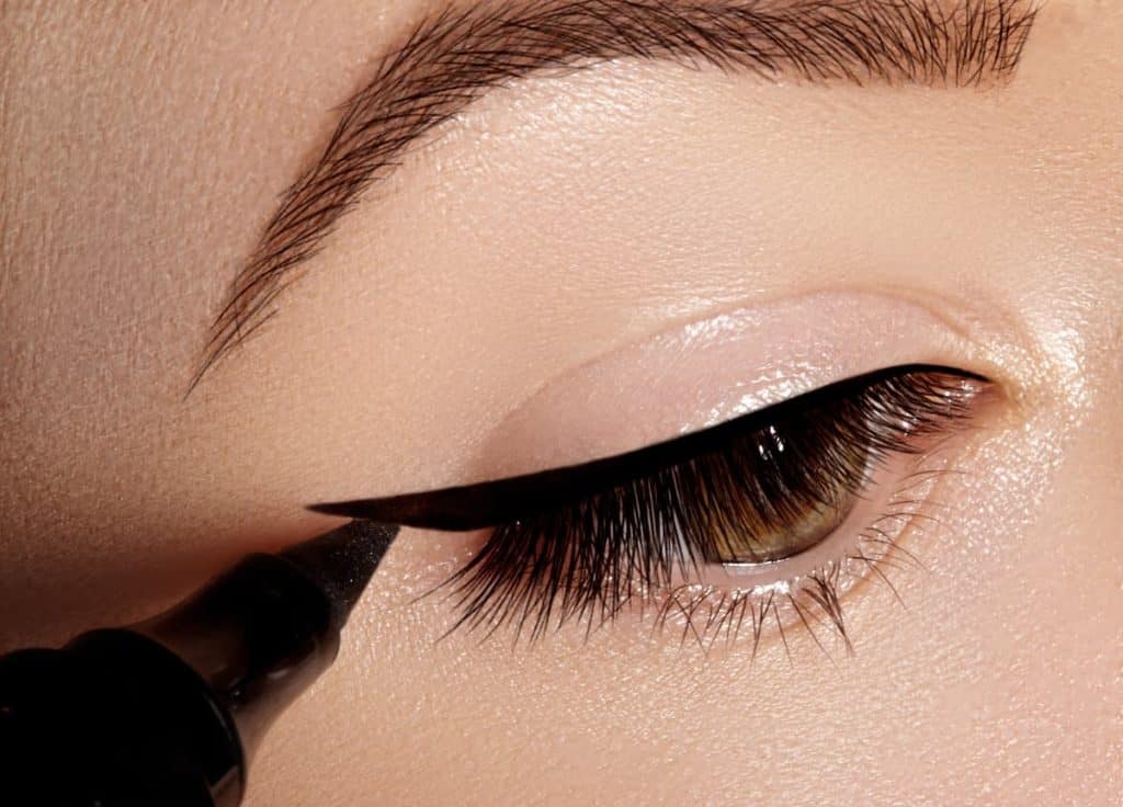 A woman is applying black eyeliner for sensitive eyes.