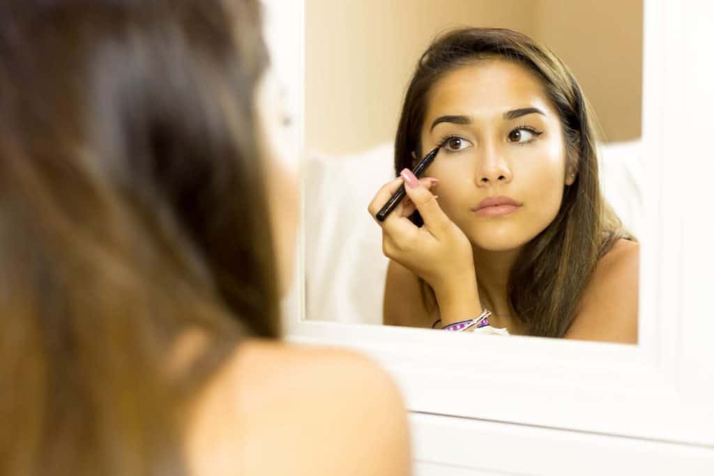 A woman applying the best eyeliner in front of a mirror.