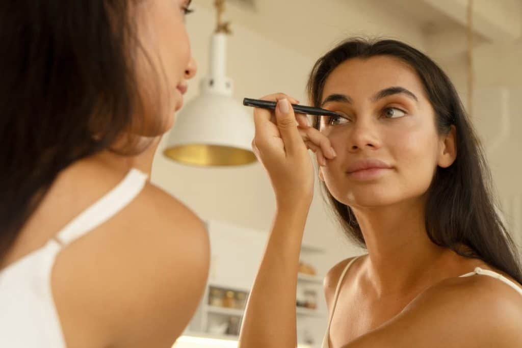 A woman applying eyeliner in front of a mirror.