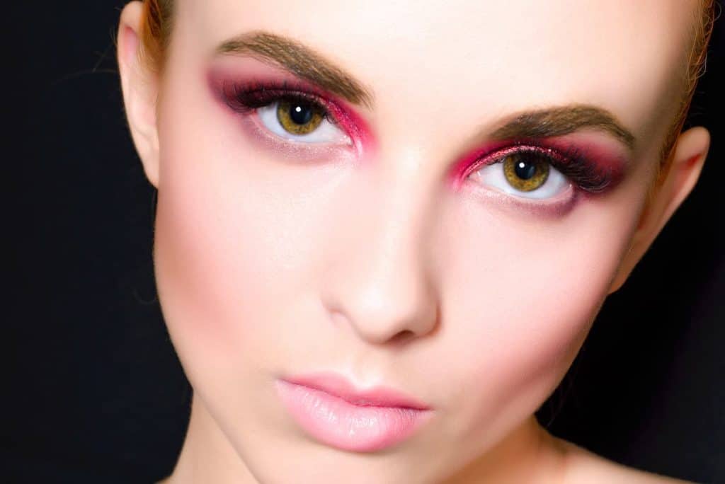 A woman with pink eye makeup and a black background.