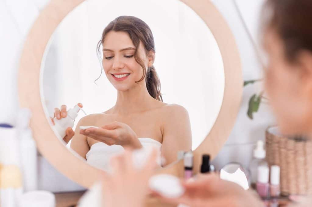 A woman is putting on her facial toner with niacinamide in front of a mirror.
