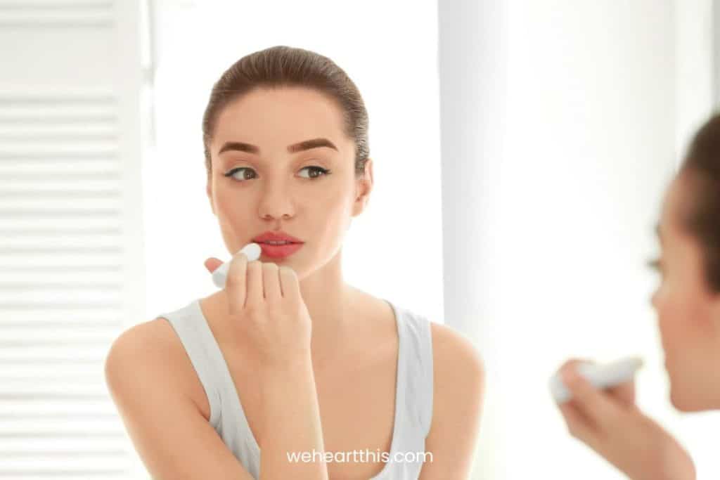 Beautiful young woman applying chapstick while looking at herself in the mirror