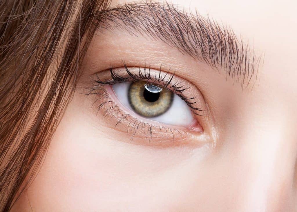 A closeup image of a woman's light hazel eye with longer eyelashes