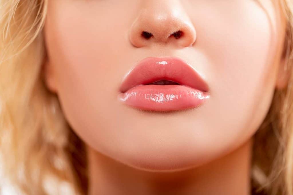 A close up of a woman's lips with glossy peach lipstick