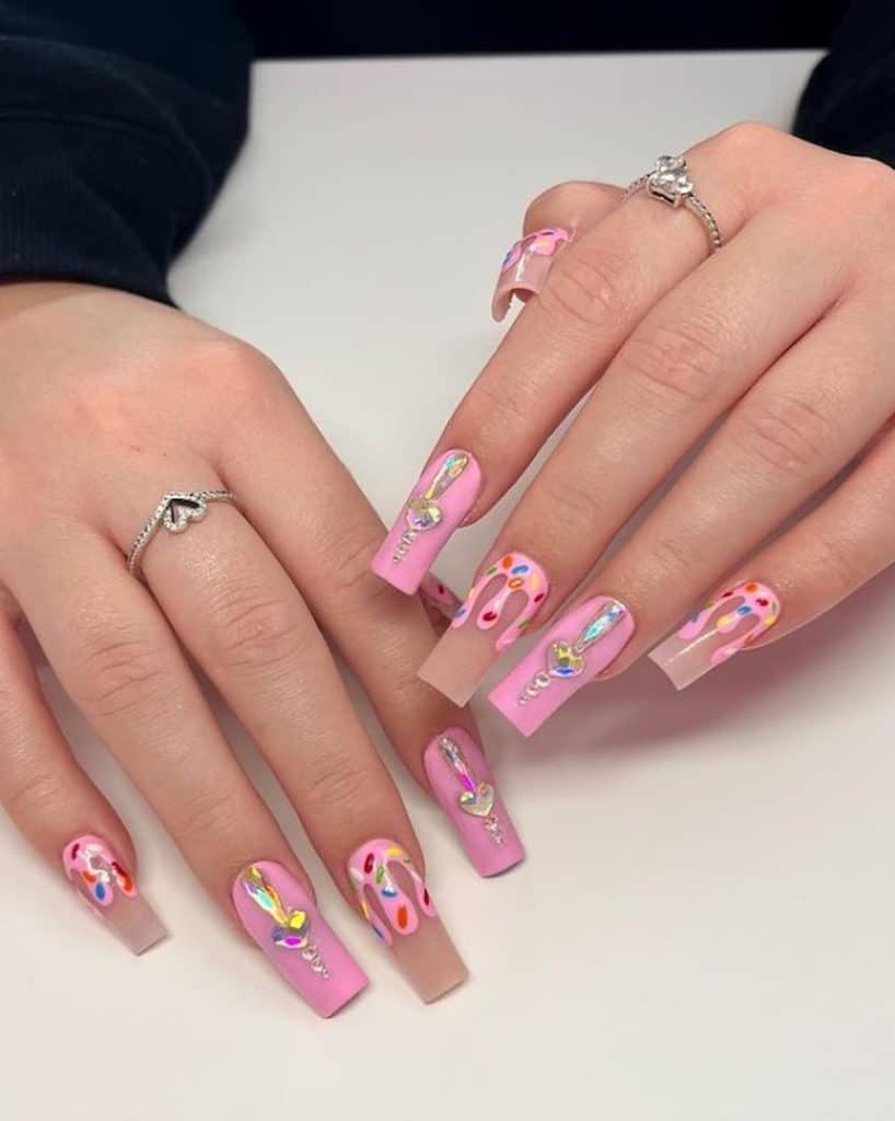 A woman's hands with pink nail polish that has rainbow sprinkles and gemstones nail designs