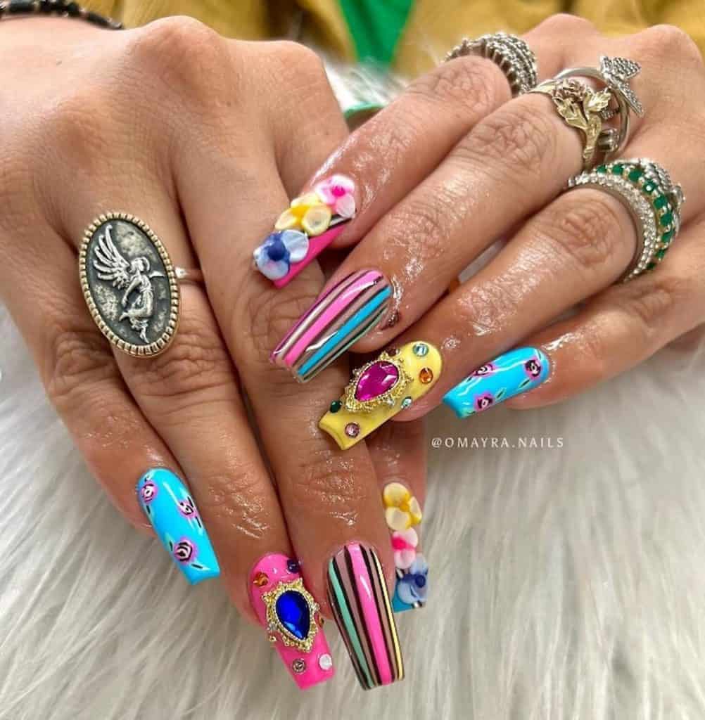 A closeup of a woman's hands with pink, yellow, and blue nail polish that has striped nail art, 3D flowers, gems, and colorful rhinestones nail designs