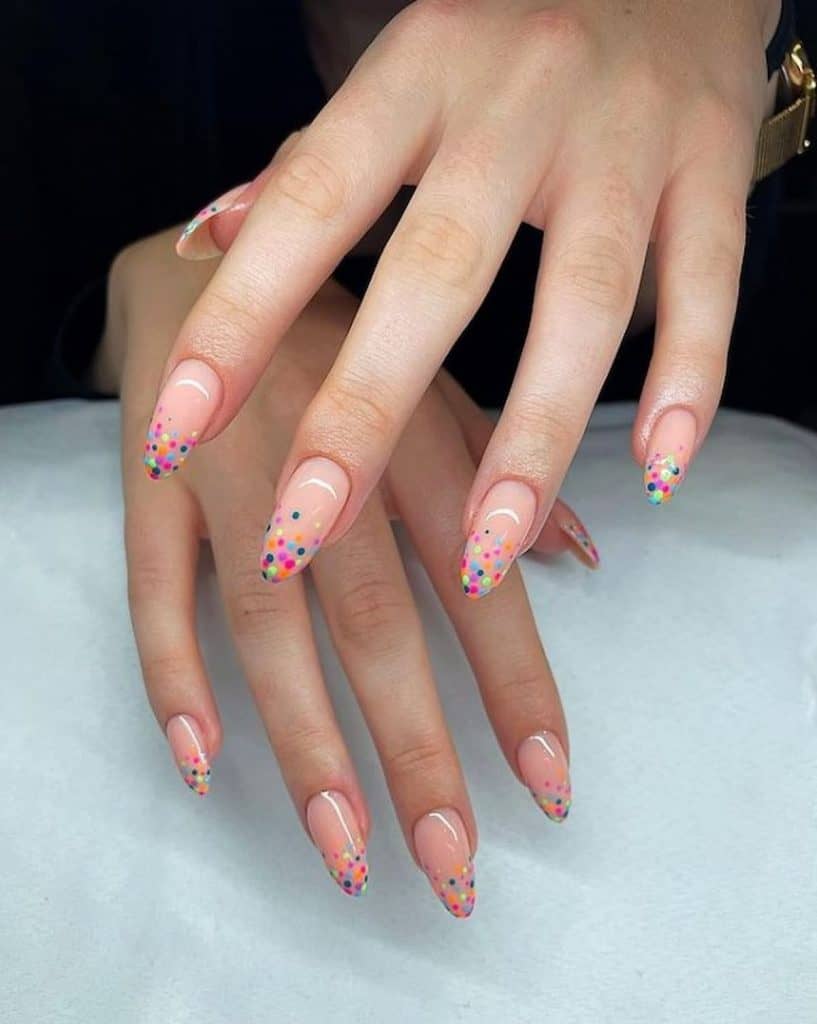 A woman's hands with beautiful pale pink nail polish base that has colorful dotted French tips