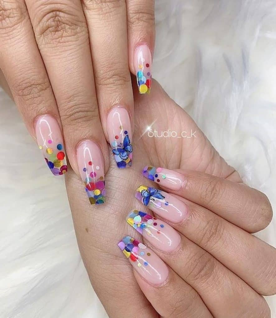 A woman's hand with a blush pink coffin nails that has colorful confetti and blue butterfly nail designs 