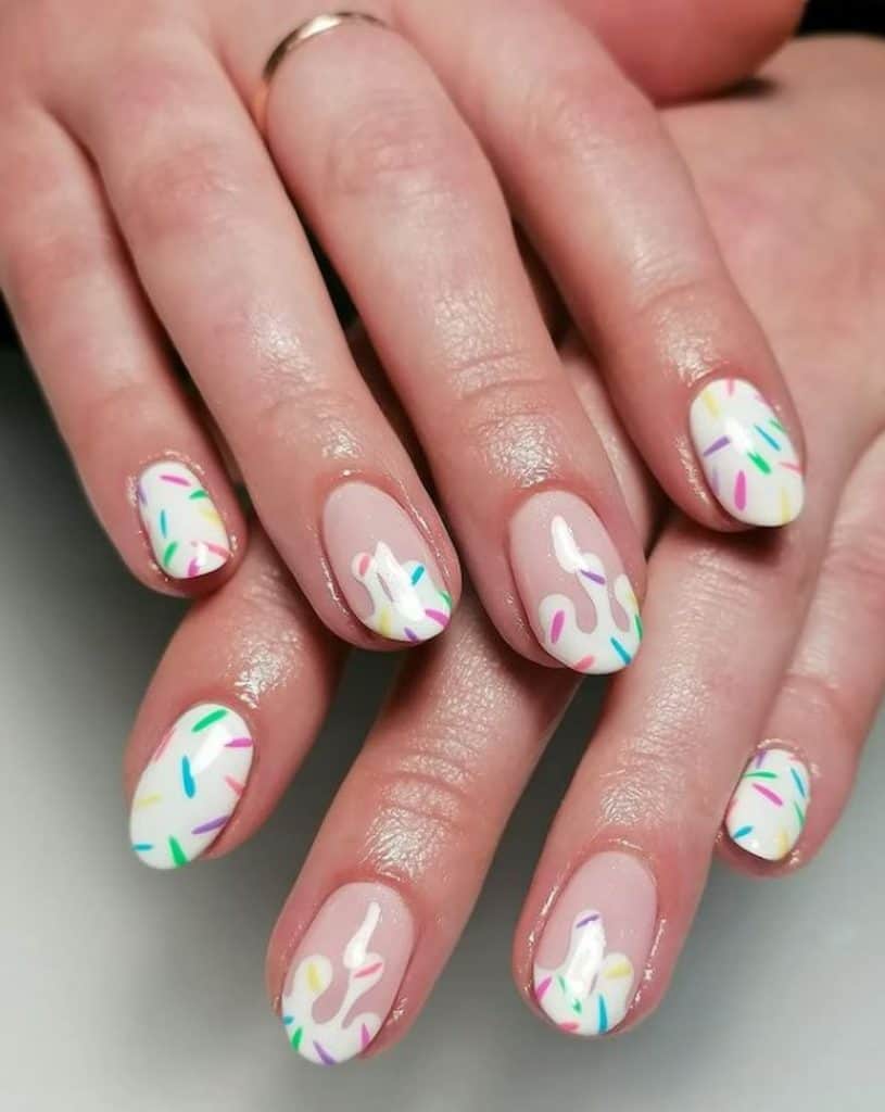 A closeup of a woman's hands with a combination of nude and white nail polish that has colorful sprinkles on top of a white nail polish