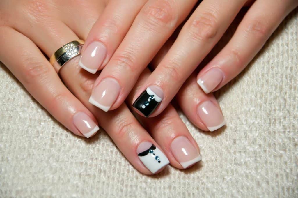 A beautiful woman's hands that has a nude polish with black and white accent nail designs and tiny gems