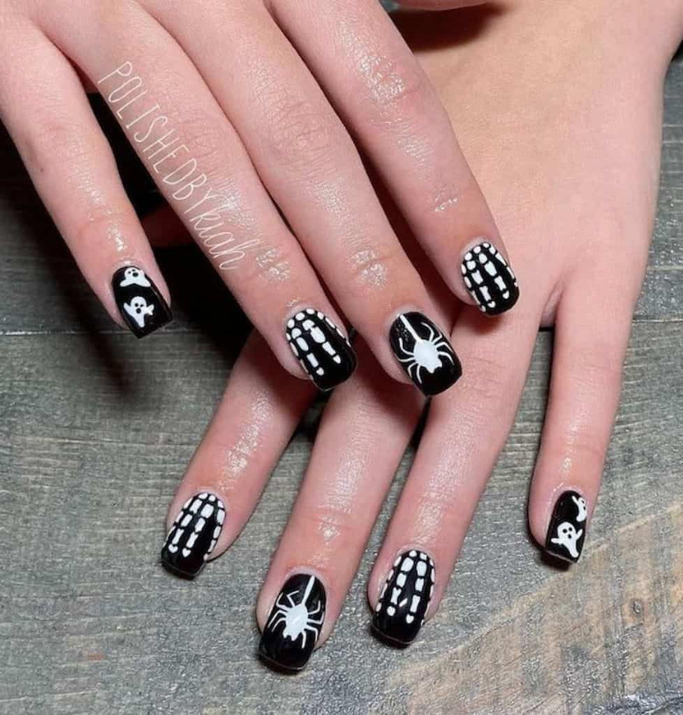 A woman's hands that has a black nail polish with white ghosts, skeleton hands, and spiders design